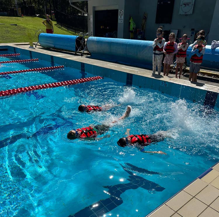Student participating in an outdoor swim school lesson, practising floating skills with confidence.