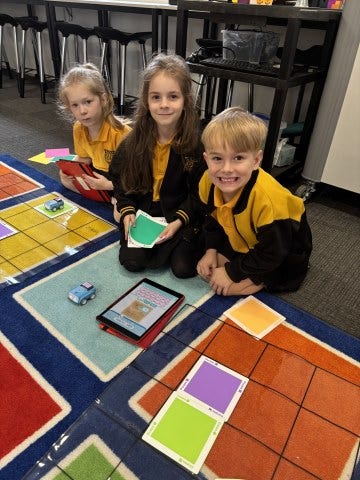 Three smiling students working with robots on a colourful classroom mat.