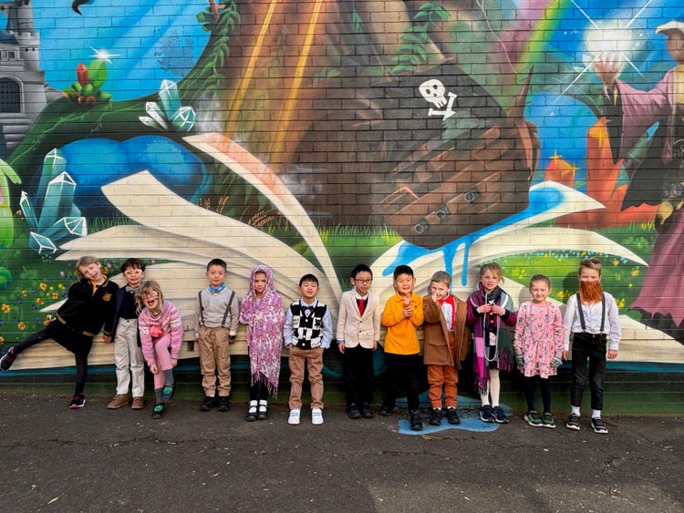 Students in 100 years old costumes in front of a colourful wall painted mural