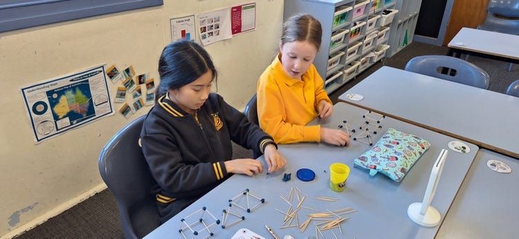Two girl students working together on a hands-on maths activity at their desk.