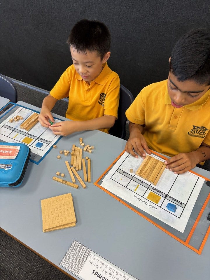 Two boys using number blocks and hands-on maths manipulatives at their desk.