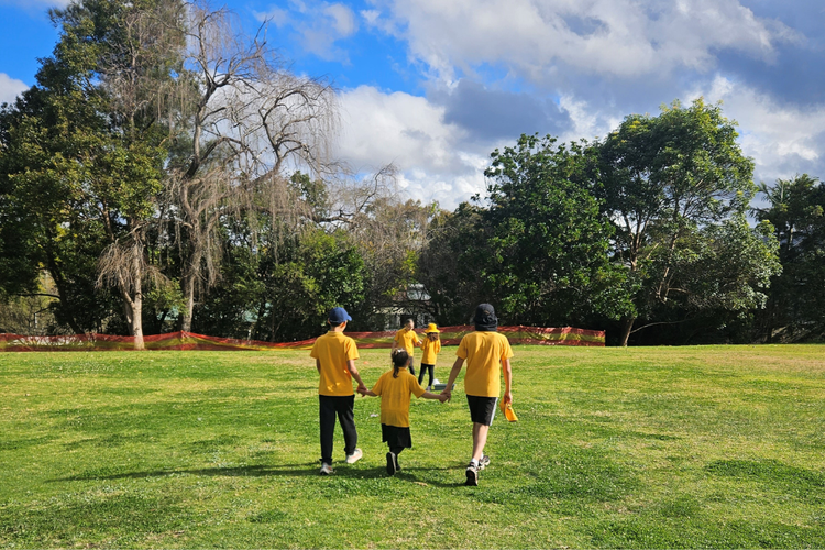 Two Year 6 students holding hands with a Kindergarten student as they walk across the school oval.