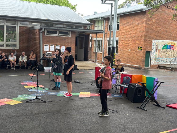 Four students performing as the school rock band during an outdoor assembly,