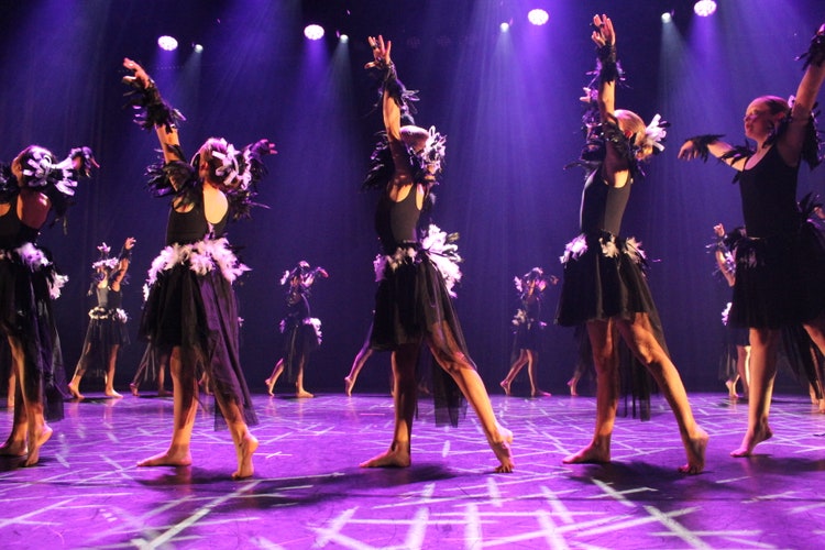 Students performing a dance on stage wearing elegant black feather costume