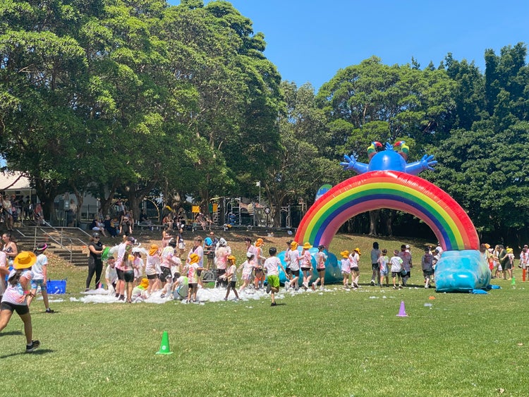 Students on the school oval running under a colourful giant balloon arch during Fun Run Day.