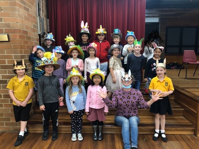 Teacher and class gathered on the school hall stage steps wearing creative Easter hats, celebrating the school’s annual Easter Hat Parade.